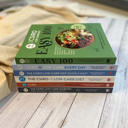 The spines of all the titles in the CSIRO Low-carb Diet series as of 2022 showing because all books are stacked on top of each other on a table