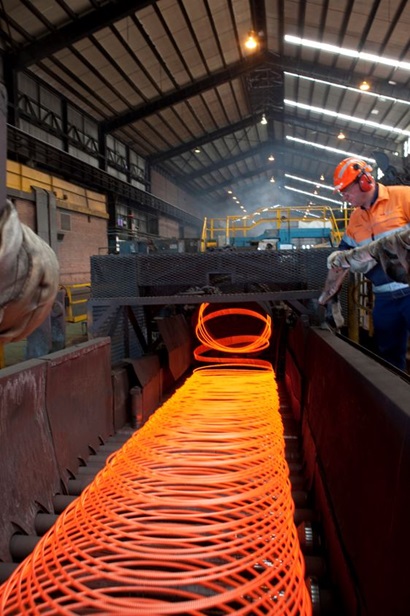 a foundry with red hot steel wire being manufactured by a man in orange PPE