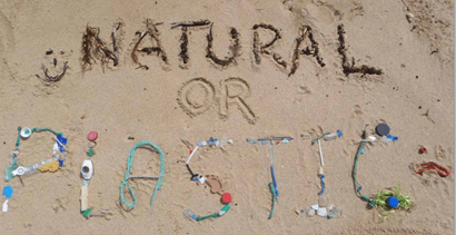 'Natural or plastic' written in the sand and with pieces of plastic
