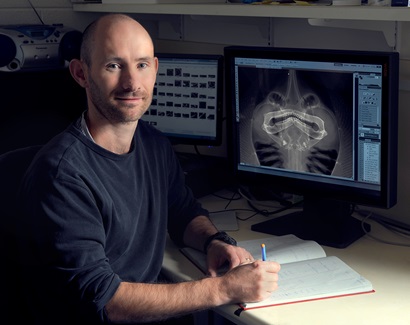 John Pogonoski sitting at desk with a screen in the background displaying a digital radiograph