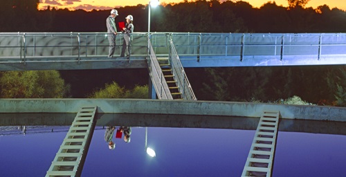 People standing on a walkway above sewage treatment tanks. 