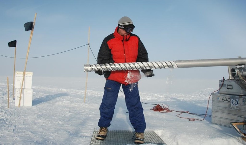 A scientist stands holding an ice core drill bit