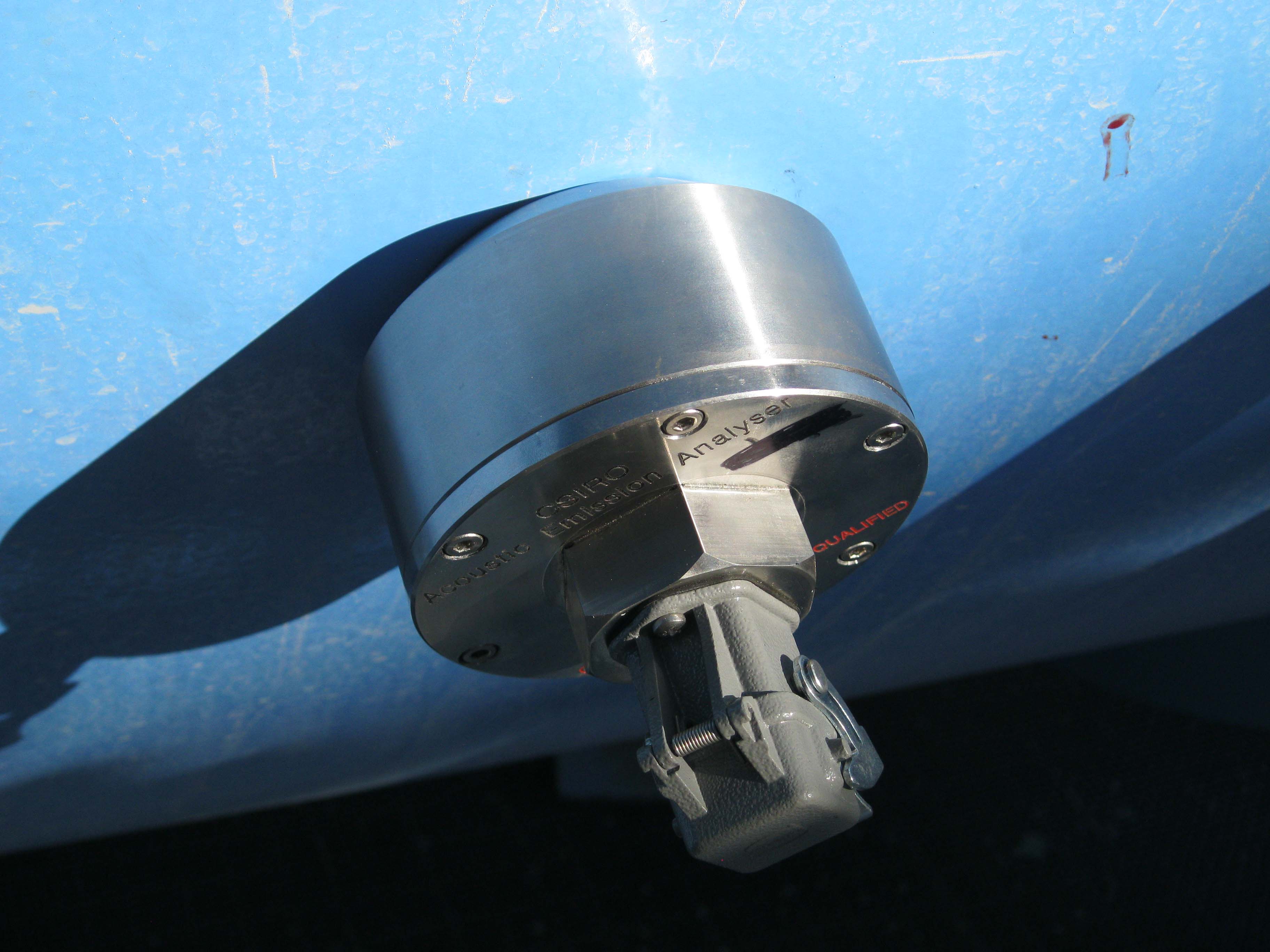 Photograph of acoustic analyser, which looks like a round metal disc, attached to a metal drum