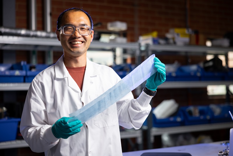 scientist standing inside a lab holding a ribbon of blue material
