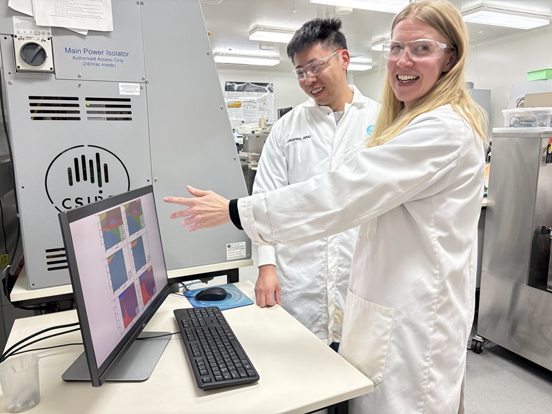 Two scientist in lab coats smiling and looking at a monitor in a laboratory 