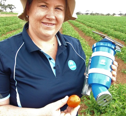 A woman in a field holding a sensor and a tomato