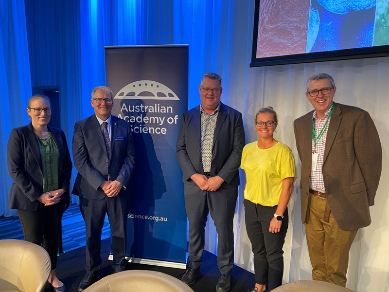 Two women and three men standing and smiling in front of the Australian Academy of Science banner