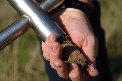 Hand holding a metal coring device, with a small soil core being tipped out