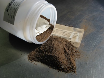 A plastic soil sample pot lies on its side with some of its contents tipped onto a table, alongside a label