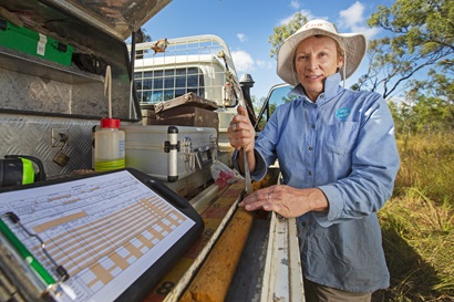 Scientist sampling soil standing next to a flat bed ute with equipment and a soil core sample.
