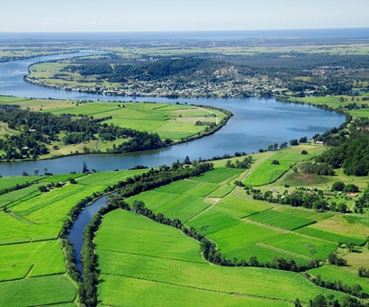 Aerial view of farmland with neatly tilled paddock and a river snaking through the landscape with a township in the distance. 