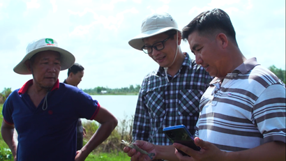 Three men in the field holding a prawn and looking at an app