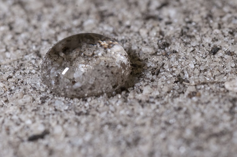 water droplet sitting on top of grey, sandy, water repellent soil