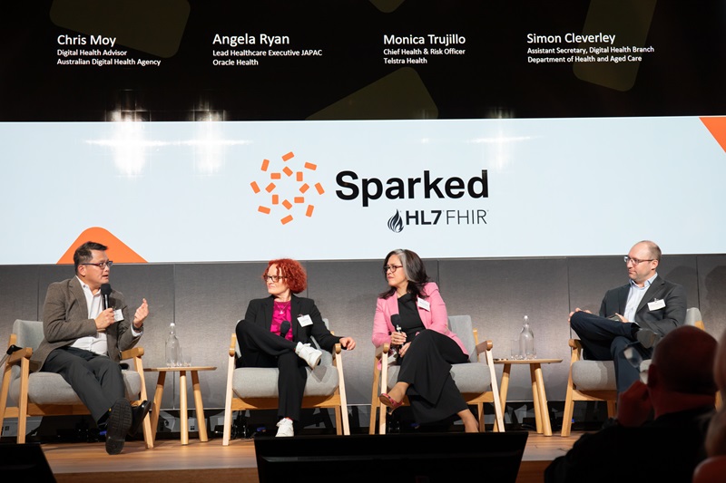 Four people on a stage at an event talking in front of a Sparked powerpoint slide