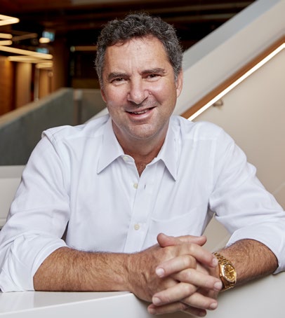 Larry Marshall smiling and leaning against a while railing with stairs in the background. 