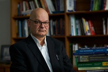 Andrew is wearing formal attire and poses against a background of books. 