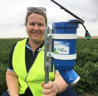 The accompanying image is a photo of Rose Brodick holding the Digiscape WaterWise device in the background. She is in a field of green crops. 