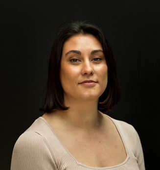 This is an portrait photo of Mibu Fischer. The image is from Mibu's shoulders up and she is standing against a black background.