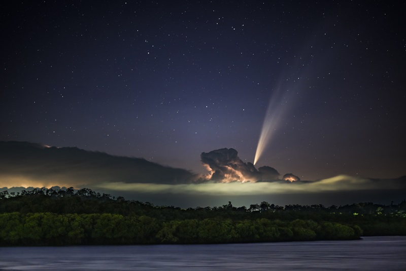 A lake, some mangroves with a glowing storm cloud overhead and a comet with long tail.