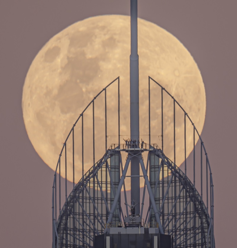 People wave from the top of a tower with a full moon behind. 