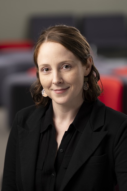 Woman with brown hair and black blazer smiles at the camera