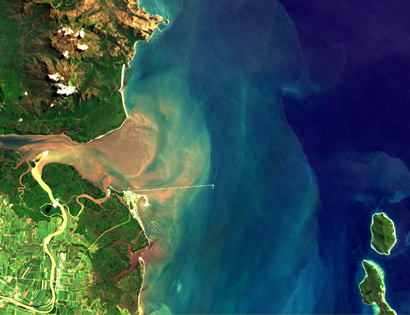 Aerial view of a river entering the ocean, with green land to the left and blue ocean to the right