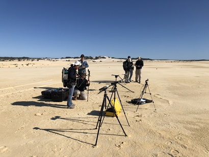 four people standing around several tripods holding various instruments in a large desert landscape.