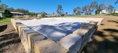 A photo outdoors, showing a 20mx20m area, bordered by sandstone blocks and filled with fine sand which is shaped to look like craters.