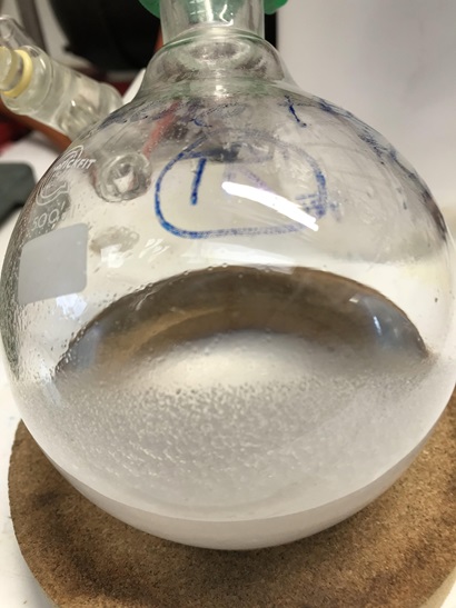Image shows a flask of extraction solution. Tiny white LiPF6 crystals of recovered material from waste batteries have formed on the inside walls of the flask.