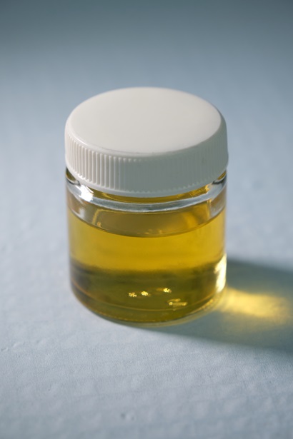 A small glass jar with a white lid sits on a white surface. Inside the jar is a golden fluid.