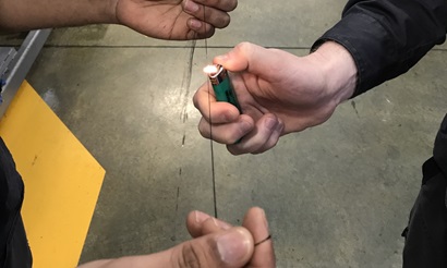 Hands holding a carbon fibre strand over a flame in a demonstration of carbon fibre robustness.