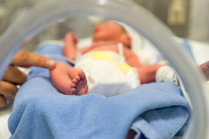 A tiny baby lies in a cot, with an adult finger reaching out to touch its knee