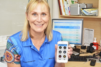 A smiling woman in a blue shirt holding an iphone displaying an app with colourful icons.