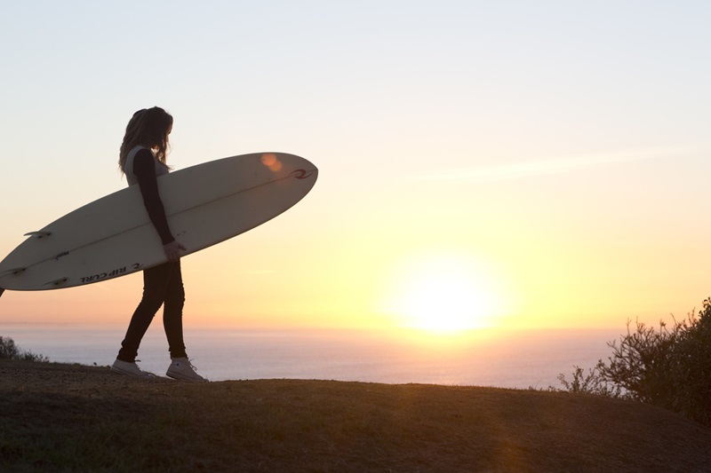 A girl holding a surfboard in front of the sunset