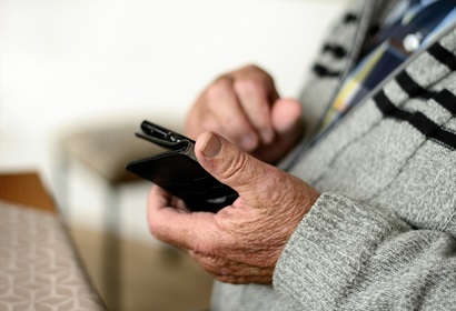 A man in grey sweater holding a black phone with a black case.