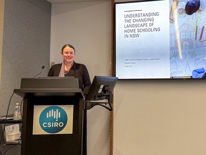 Person standing at a lectern with a CSIRO logo, presenting in front of a screen displaying a slide.