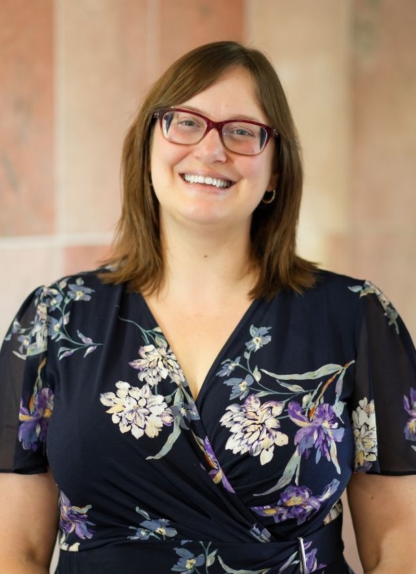 A female in floral shirt smiling and standing in front of a sandstone background.