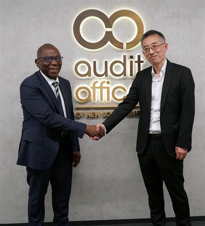 Two people in business attire shake hands in front of a wall displaying the 