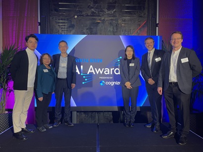 Seven people stand on a stage in front of a large screen displaying 