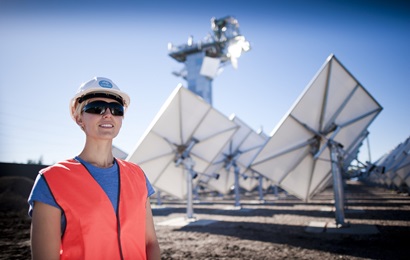 Woman stands in front of solar array wearing a hard hat and dark glasses