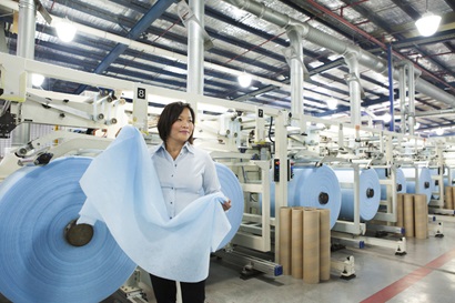 CSIRO staff member in factory at Textor Technologies production facility with moisture-trapping fabric co-developed with CSIRO. Rolls of fabric in background.