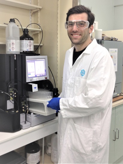 male scientist in white lab coat works on a machine in laboratory and smiles at camera