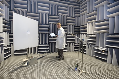 Researcher in lab coat standing in anechoic chamber testing a smoke alarm sound
