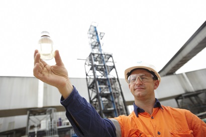 Researcher in a high-visibility shirt and a hard hat holding a clear bottle of chemical solvent