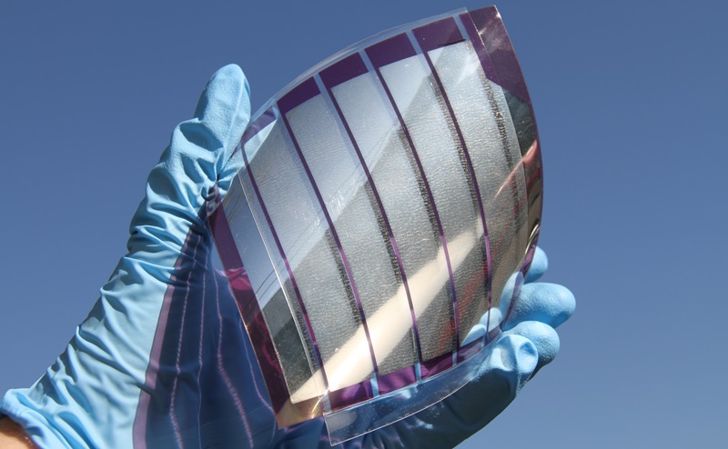 A gloved hand holding a flexible solar cell so that it bends slightly.