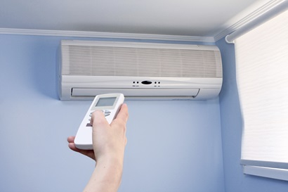 A hand holding a remote control, pointed at a wall mounted air conditioning unit.