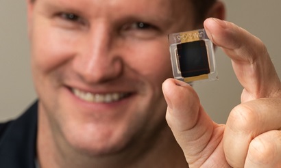 Smiling man holding small square solar cell in foreground