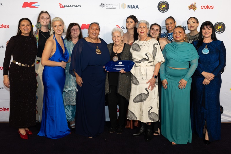 Group of women standing together with one woman holding a glass award 