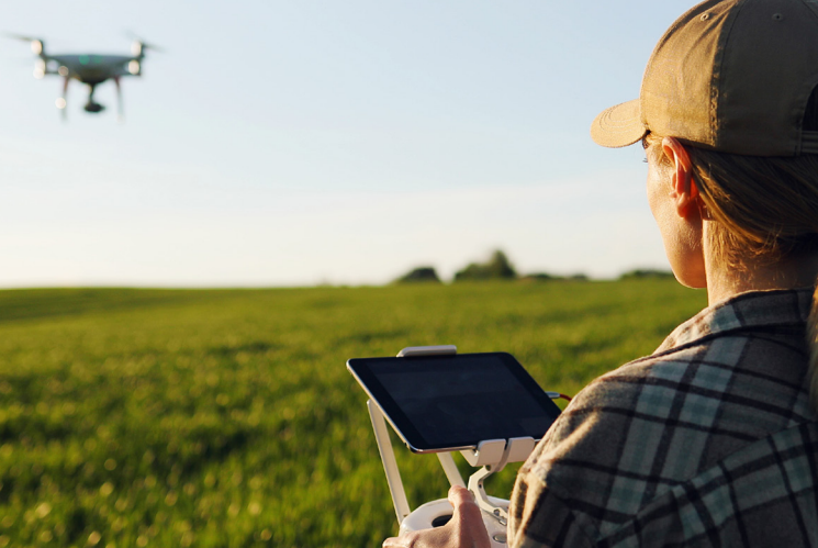 Person holding controller for drone as it flies across green pasture.