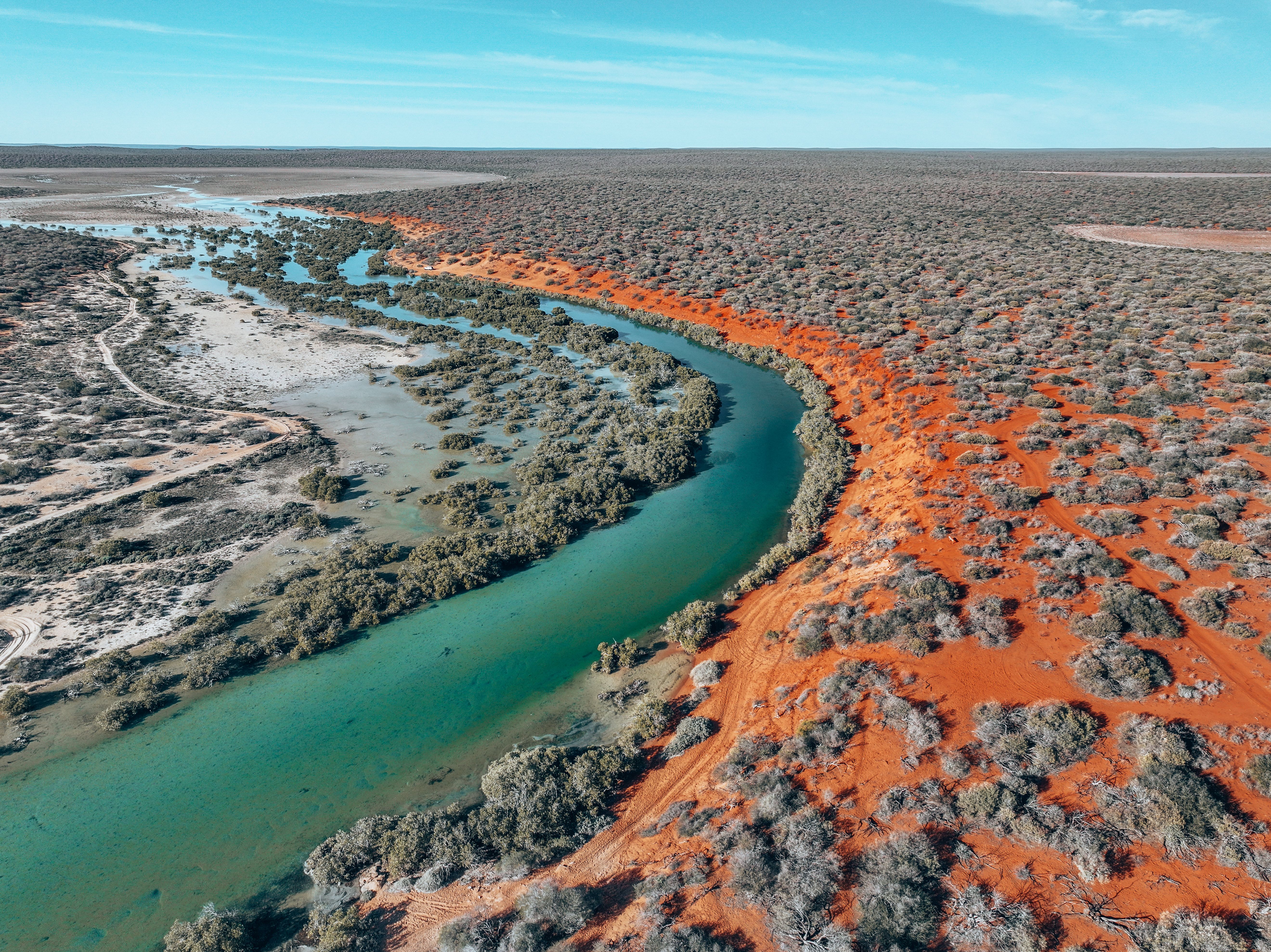 A photograph of a winding river flowing through a contrasting landscape with vibrant red soil on one side and sparse vegetation on the other.